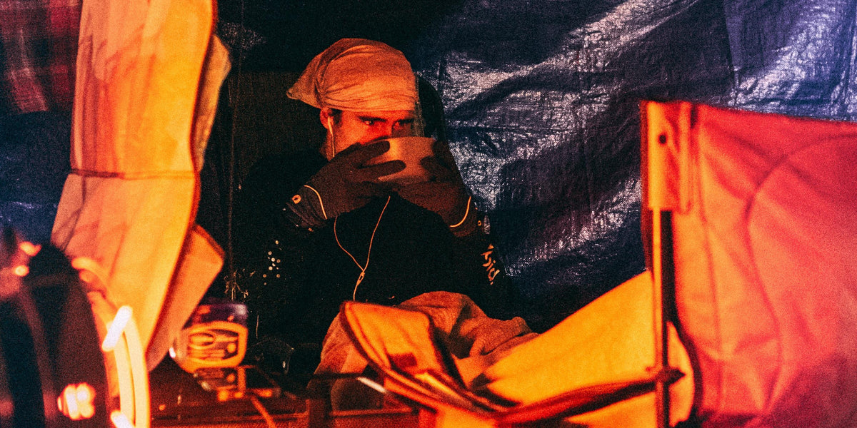Runner in warm orange light inside a tent, wearing a head covering and gloves.