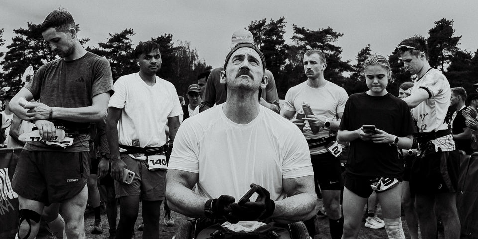 Runners gathered at an outdoor event, with an athlete in a racing wheelchair in the center.
