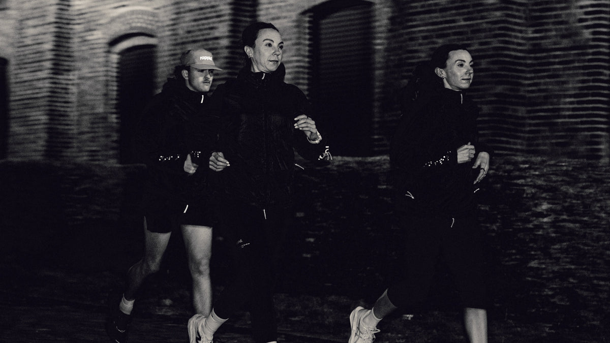 Runners wearing rappid. winter layers in front of a brick building.